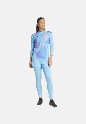 Lichtblauwe sportoutfit met een longsleeve-top met geometrische patronen en aansluitende leggings. Zwarte schoenen maken de look compleet.