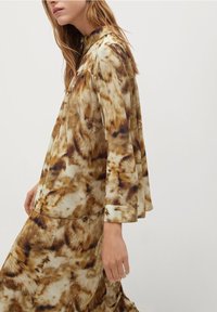 Langärmliges Oberteil mit hohem Kragen und Rock aus einem cremigen Stoff mit einem braunen und beigen abstrakten Muster, mit einer lockeren Silhouette und weicher Textur.