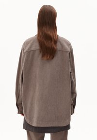 Braune Corduroy-Übergangsjacke im Oversized-Stil mit geradem Saum, langen Ärmeln und einem Rückenpasse-Detail. Texturiertes, weiches Material mit vertikalen Rillen.