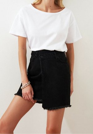 Vrouw in een eenvoudige witte t-shirt met korte mouwen, ingestopt in een zwarte asymmetrische denim minirok met een rafelige zoom en een zilveren kettingarmband.