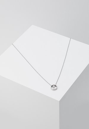 Collier en argent avec un pendentif circulaire orné d'une pierre claire centrale, suspendu à une chaîne délicate, présenté sur un socle blanc.