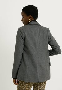 Blazer gris sur mesure en tissu texturé, doté d'un col cranté, de manches longues et d'une fente arrière pour la mobilité.