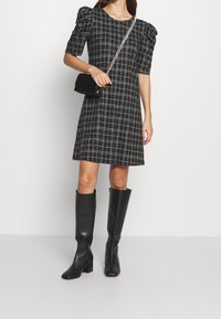 Vestido de cuadros en negro con mangas cortas abombadas, combinado con botas de cuero negras hasta la rodilla y un mini bolso cruzado con correa de cadena.