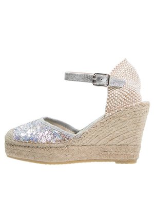 Klínová espadrilová obuv se stříbrným třpytivým svrškem, elastickým páskem kolem kotníku a tkanou podešví z juty. Obsahuje světle šedou podšívku a texturované detaily.
