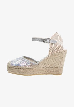 Koturny espadryle z srebrzystą połyskującą cholewką, elastycznym paskiem wokół kostki i plecioną juty podeszwą. Charakteryzują się jasnoszarym podszyciem i teksturowanymi akcentami.