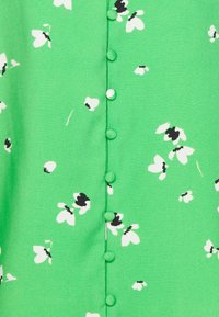 Tessuto verde con piccoli motivi floreali neri e bianchi, con una fila centrale di sei bottoni rivestiti in tessuto coordinato.