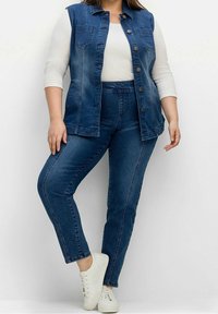 Denimväst i mörkblått med knappstängning och framfickor, i kombination med högmidjade mörkblå jeans. Vita sneakers fulländar looken.