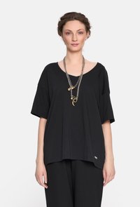 Czarna, oversize koszulka z miękkiego materiału, z szerokim dekoltem i krótkimi rękawami, ozdobiona subtelnym detalem logo blisko dołu.