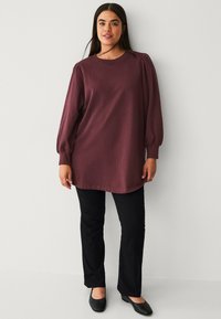 Bordeaux lange mouw tuniek met een ronde halslijn en pofschouders, gecombineerd met zwarte flared broek en zwarte platte schoenen.
