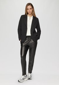 Zwarte blazer met twee knopen, witte top met rits in de hals, zwarte leren joggers en zilveren sneakers met zwarte accenten. Gladde textuur overal.
