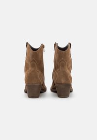 Botines de ante marrón con un diseño western, que presentan costuras decorativas, un tacón de bloque de altura media y un cierre de cremallera a los lados.