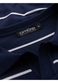 Námořnická polokošile s bílými horizontálními pruhy, texturovaná tkanina a žebrovaný límeček. Štítek nese nápisy "ombre" a "QUINTESSENCE."