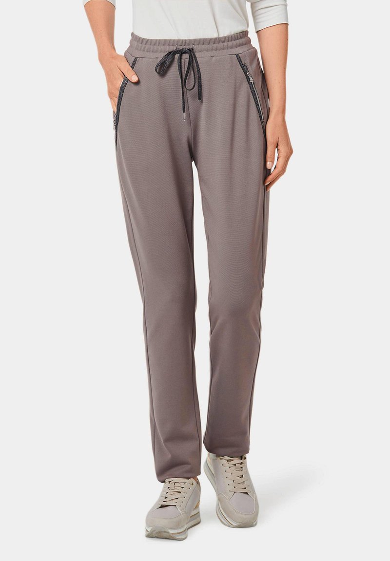 Graue Sporthosen mit Kordelzugbund, seitlichen Reißverschlusstaschen und strukturiertem Stoff, kombiniert mit hellen Turnschuhen.