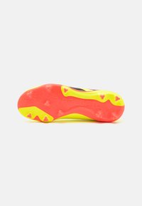 Sole di scarpini da calcio nera con accenti gialli e rossi luminosi. Presenta una superficie testurizzata e tacchetti di trazione distintivi per una migliore aderenza.