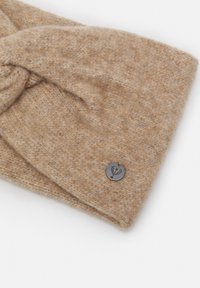 Bandeau en laine tricotée marron, avec une texture douce et un design torsadé. Présente un petit accent en métal rond comme logo sur un côté.