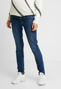 Blue denim jeans with a slim fit design, featuring five pockets and light whiskering. Paired with a cream sweater and white sneakers.