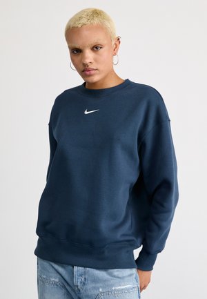 Sudadera azul marino hecha de una mezcla de algodón, con cuello redondo y un pequeño logo blanco de Nike en el pecho. Textura suave con puños acanalados.