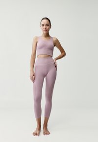 Svetloružový športový podprsenka a vysoké legíny s rebrovanou textúrou a detaily švov, ktoré predvádzajú priliehavý dizajn.
