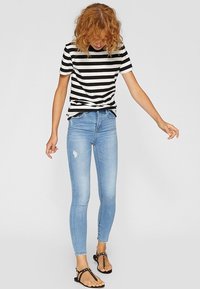 Camiseta de manga corta a rayas en blanco y negro, combinada con jeans skinny de color azul claro con detalles desgastados y sandalias planas negras.