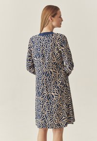 Marineblaues Kleid mit beigem Blattmuster, langen Ärmeln, knielanger Silhouette, rundem Ausschnitt und weichem Stoff. 