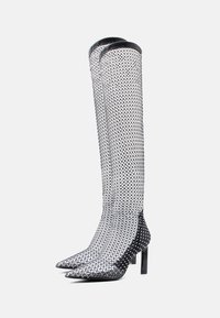 Μαύρες μπότες δίχτυ έως το γόνατο με μυτερές μύτες, λεπτά ψηλά τακούνια και μοτίβο διαμαντιού, με γυαλιστερό φινίρισμα στη μύτη και στη φτέρνα.