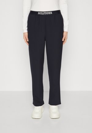Pantaloni sportivi blu navy realizzati in un tessuto morbido con cintura elastica, con la scritta "HILFIGER" in bianco, abbinati a sneaker bianche.