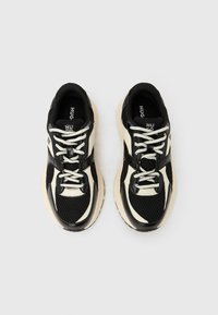 Μαύρα και μπεζ αθλητικά παπούτσια με υλικό από δίχτυ, επενδυμένο γιακά, αντίθετες λεπτομέρειες και χοντρή λαστιχένια σόλα. Τα κορδόνια είναι λευκά.