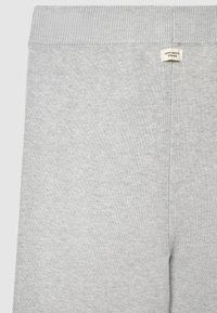 Graue Jogginghose aus weichem Stoff, mit einem gerippten Bund und einem Etikett mit der Aufschrift "ZERO WASTE DESIGN" nahe der Taille.