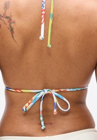 Τοπ μπικίνι πολύχρωμο με λεπτές τιράντες στο πίσω μέρος, με μπλε, κόκκινα, κίτρινα και πράσινα σχέδια σε λείο ύφασμα. Προσφέρει μοναδικό σχέδιο.