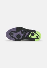 Suela de goma negra con detalles en púrpura y verde, presenta patrones texturizados y elementos circulares para mejorar la tracción. Logo de Puma visible.