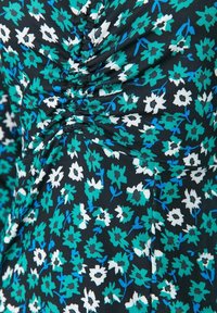 Gros plan d'un tissu noir avec un motif floral en petites fleurs teal, blanches et bleues, et un détail de couture froncé au centre.