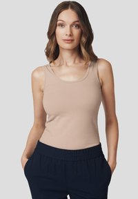 Jasno beżowa, bezrękawnikowa koszulka z okrągłym dekoltem, wykonana z miękkiego, elastycznego materiału, w połączeniu z ciemnoniebieskimi spodniami na elastycznej talii.