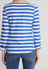 Blau-weißer gestreifter Langarmshirt mit rundem Halsausschnitt und aufgerollten Ärmeln, kombiniert mit Jeans. Glatte Textur, lässiges Design.