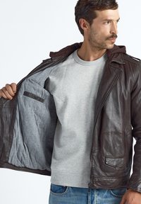 Ruskea nahkatakki, jossa on vetoketjullinen edessä, harmaa kangasvuori ja huppu. Ominaisuuksiin kuuluvat sivutaskut ja rintatasku.