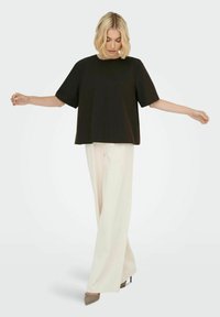 Sort kortærmet top med en afslappet pasform, parret med kræmfarvede, vide bukser og beige hæle, mod en neutral baggrund.