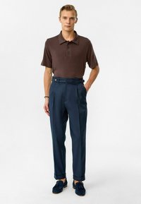 Bruine poloshirt met een kraag en drie knopen, gecombineerd met hooggesneden marineblauwe broek met twee zijknopen en opgerolde manchetten.