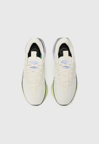 Chaussures de sport blanches avec une partie supérieure texturée, une semelle vert clair, des accents gris, et des lacets proéminents avec un logo sur la languette.