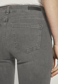 Šedé džíny z denimu s přiléhavým střihem, vybavené jednou zadní kapsou, jemným prošíváním a černou koženou nášivkou na pase.