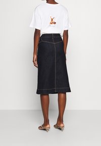 Tmavě modrá denimová midi sukně se světlým prošitím, s mírně vykrojeným lemem a zadním rozparkem. V kombinaci s bílým tričkem s grafickým potiskem.