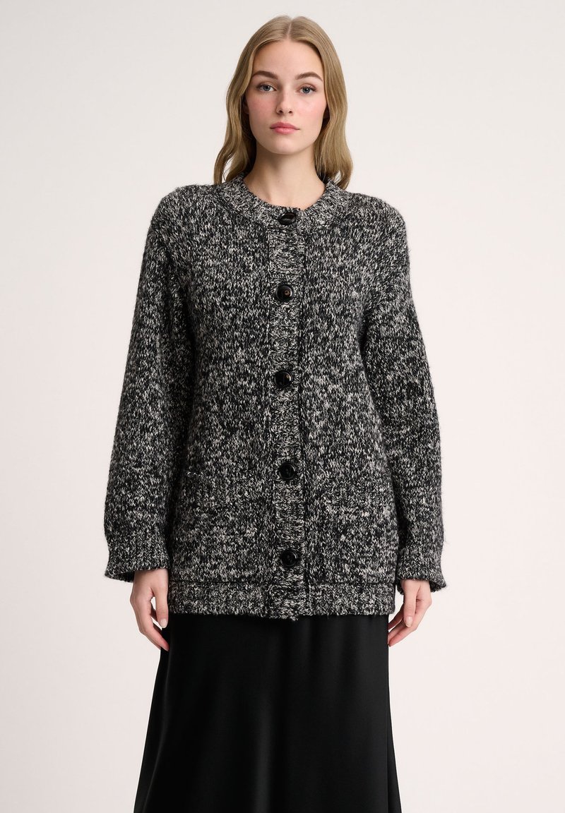 Gebreide zwart-witte cardigan met een ronde halslijn, knopen aan de voorkant en lange mouwen. Zachte textuur met een chunky, gebreid patroon.