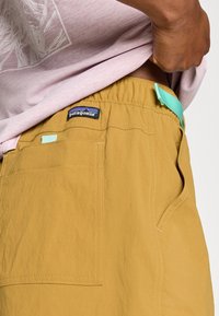 Καφέ χακί σορτς με υφή, ελαστική μέση και λεπτομέρεια σε μέντα πράσινο. Διαθέτει λογότυπο και πλαϊνή τσέπη.