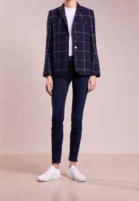 Marinblå rutig kavaj med två knappar, enkel bröstficka och slagkrage, parat med mörka jeans och vita sneakers.