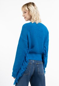 Maglione azzurro lavorato a maglia con dettagli frangiati, caratterizzato da un design comodo e un tessuto testurizzato, abbinato a jeans di denim a vita alta.