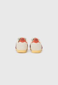 Röda och beige sportskor med texturerad ovandel, gummisula och orange detaljer på hälen, som visar en retrodesign.