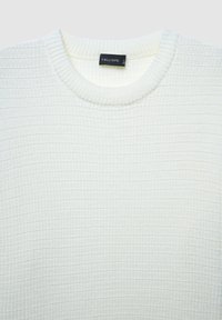 Maglione bianco lavorato a maglia con una texture a coste, scollo rotondo e un'etichetta con la scritta "CALLIOPE." Presenta un aspetto morbido e caldo.