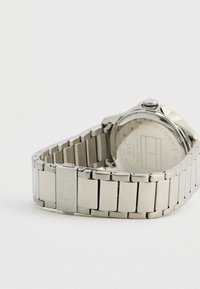 Hõbedane metallist kellarihm ja lukustus, millel on graveeritud logo, osaliselt nähtav kellakorpuse tagakülg valgel taustal.