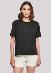 Schwarzes Baumwoll-T-Shirt mit Rundhalsausschnitt und kurzen Ärmeln, in lockerer Passform, kombiniert mit hellen Shorts.