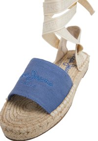 Sinine kangast espadrill, millel on punutud jute tald; omaduseks kreemikarva satiinstrapid koos reljeefse logoga. Avatud varvastega disain, sile tekstuur.