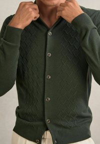 Cardigan verde închis dintr-o țesătură texturată, cu un model în diamant, cinci nasturi și manșete și tiv cu nervuri.