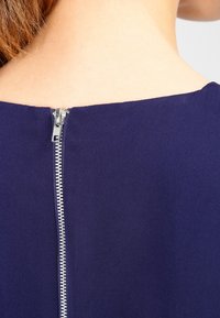Navy blue fabric with a smooth texture, featuring a silver metal zipper at the back, extending from the neckline to the mid-back.